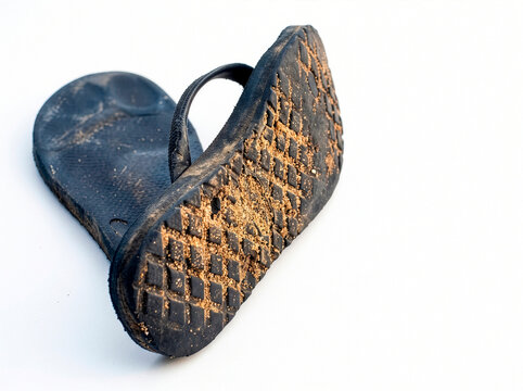 A pair of black flip-flops covered in dirt, with one sandal flipped upside down to show the sole