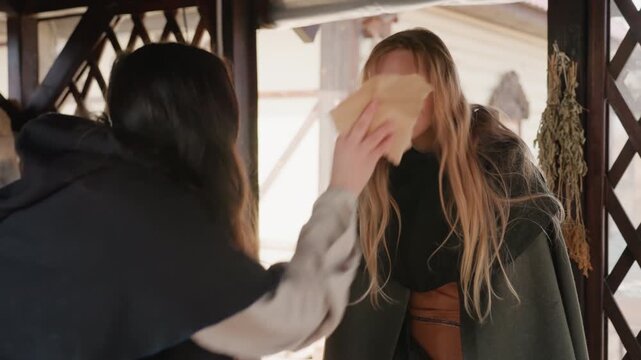 Two women exchange document inside wooden pavilion with warm side daylight, one standing with braids smiling while other leans forward offering paper, creating calm friendly interaction