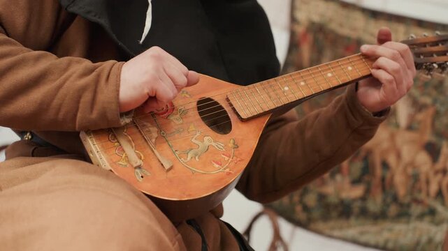 Person playing a stringed instrument playing the instrument, in indoor setting with patterned fabric in the background, with stringed instrument, patterned fabric, with brown, black accents.