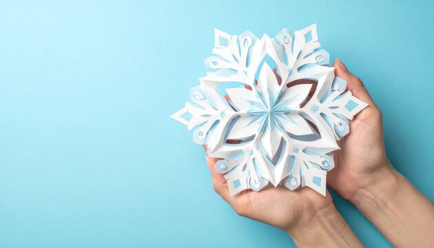 Paper snowflake handmade decoration winter holiday craft held by human hands on blue background