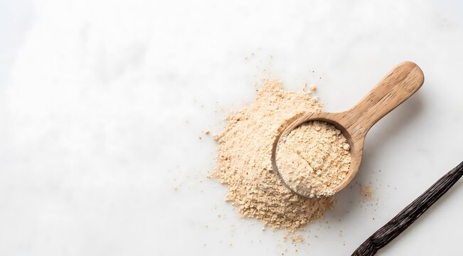 Clean minimalist product photograph of a small mound of fine pale tan vanilla powder on a smooth white marble surface, with a wooden measuring scoop resting beside it half-filled with powder. 