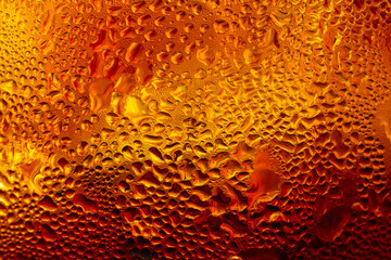 Close-up of condensation water drops on a cold glass of golden beer or beverage,Macro texture background of cold water droplets and condensation covering the surface of a chilled glass with a warm gol © banjongseal324