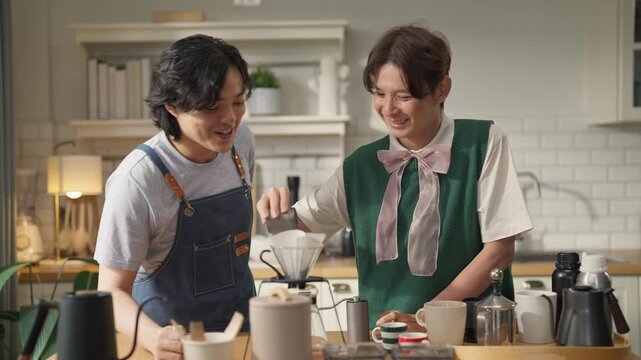 Man in denim apron smiling while brewing pour-over coffee, teaching friend at home kitchen counter, coffee beans and drip equipment on table, weekend hobby and hospitality concept, warm morning light.