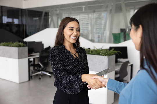 Happy Arabian businesswoman greeting client or colleague with handshake gesture. HR manager welcoming vacancy applicant standing together in contemporary co-working space, expressing mutual respect