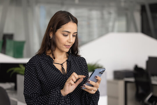 Focused Middle-Eastern businesswoman using smartphone at modern workplace, checking work emails, replying client messages, scheduling meetings, managing tasks or to-do list or making business calls