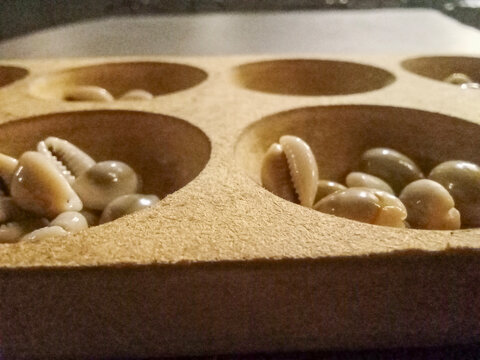 Perspective view of traditional Indonesian Congklak mancala game board with cowrie shell pieces