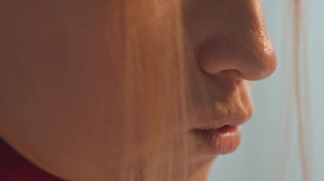 Close up of young woman with long blonde hair speaking softly. Detailed facial features like nose lips chin captured. Intimate close up emphasizes subtle expressions