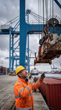 Dock worker with radio guiding a gantry crane spreader at container terminal