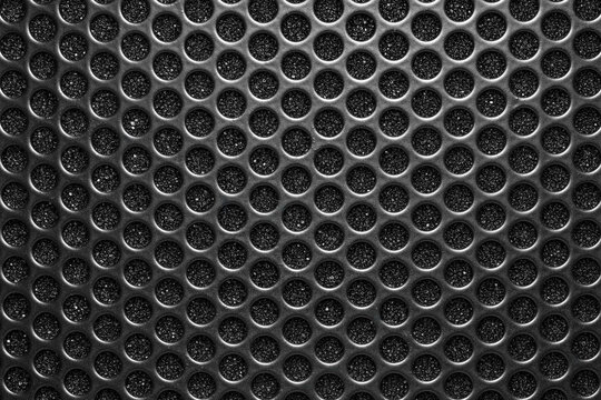 The lighting is dramatic, with strong highlights on the raised edges of the perforations and deep shadows within the holes.