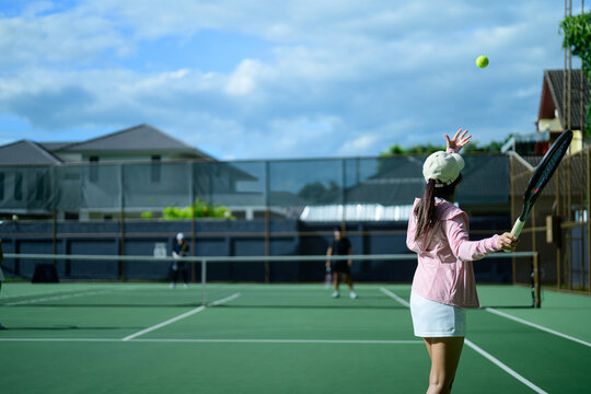 Young Asian Woman Serving Tennis Ball on Outdoor Green Court During Sunny Day