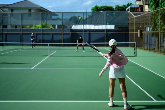 Young Asian Woman Playing Tennis on Outdoor Green Court with Friends on a Sunny Day