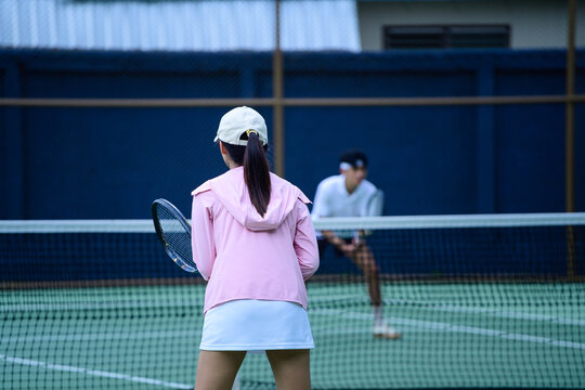 Young Asian Woman Playing Tennis on Outdoor Court with Partner Across the Net