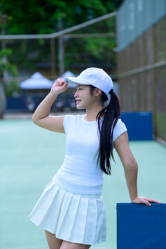 Young Asian Woman in White Tennis Outfit on Court Adjusting Cap with Confident Smile