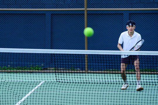 Young Man Playing Tennis at Net on Outdoor Court Ready to Hit Incoming Ball