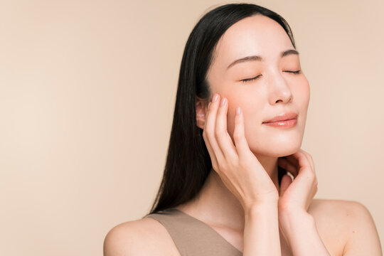 顔に手を添える黒髪ストレートヘアの若い日本人女性。スキンケアイメージ。