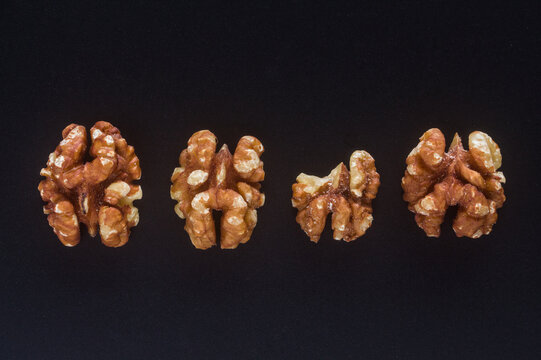 Four walnut kernel halves in a row on a black background