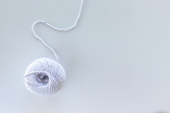 White yarn ball with thread curving on a white background