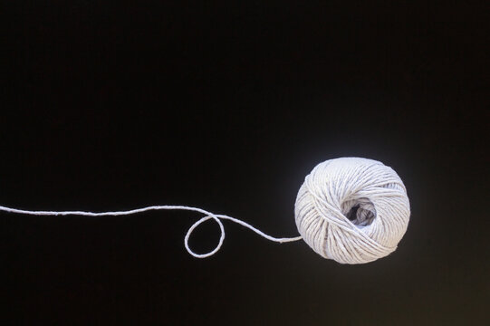White yarn ball with a long thread on a black background