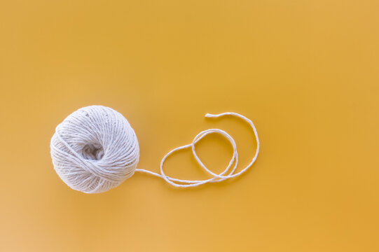 White yarn ball with looped thread on a yellow background