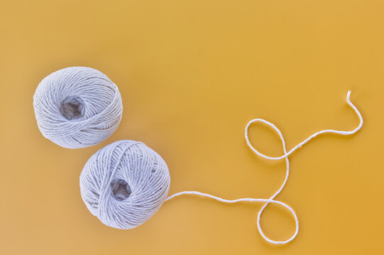 Two white yarn balls with looped thread on a yellow background