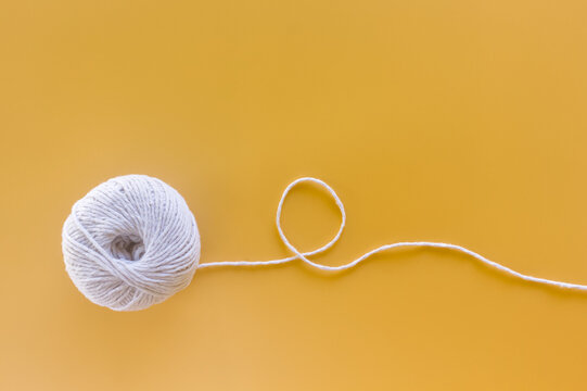 Ball of white yarn with a wavy thread on a yellow background