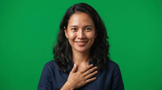 Sincere Smiling Asian Woman with Hand on Her Heart Expressing Gratitude and Honesty on Green Background
