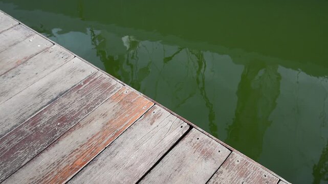 edge of weathered hardwood deck and pier beside calm canal with reflections
