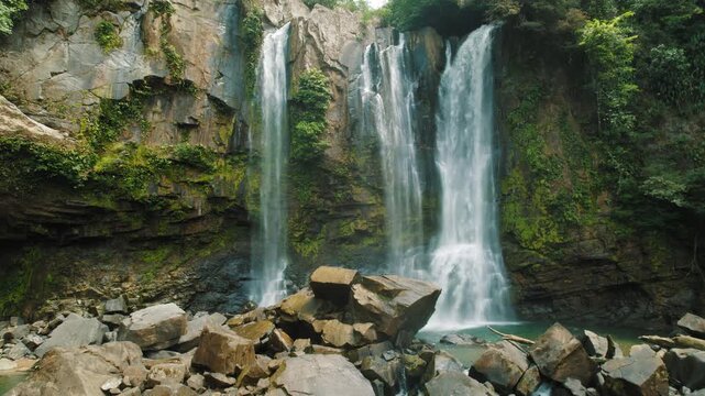 Close view of tall tropical waterfalls cascading over rocky cliffs into pool