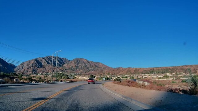 Point-of-view shot filmed from a moving car on a highway with distant mountains visible in the background, in Los Angeles, California. Filmed during midday with bright sunlight. No audio.