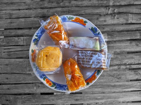 Top view of traditional Indonesian snacks or jajanan pasar served on a floral ceramic plate over a black and white rustic bamboo table with selective color effect