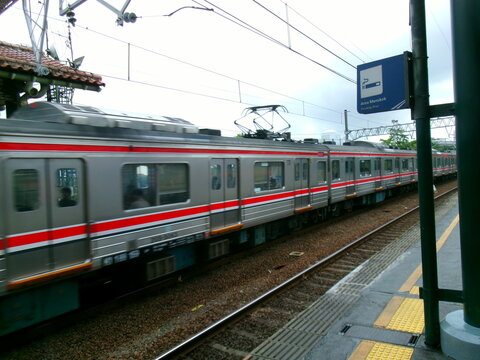 Commuter train passing a station with red-tile roof and smoking sign
