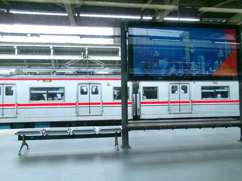 Commuter trains at a platform beside a city skyline advertising screen