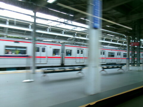 Silver commuter train with red stripe passing a station platform