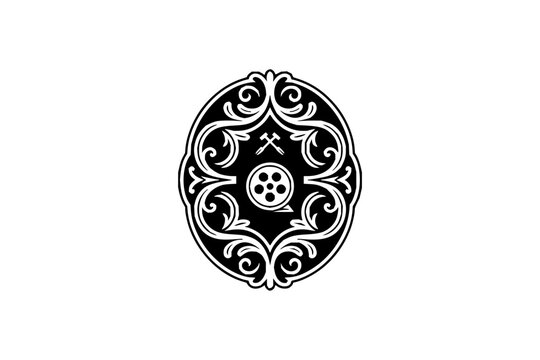 Ornate movie production guild emblem featuring a film reel and crossed hammers set against a black oval background with white decorative filigree