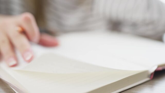 Unrecognizable female student writing in notebook turning blank paper page searching for information. Close up shot of person browsing a journal, diary or textbook
