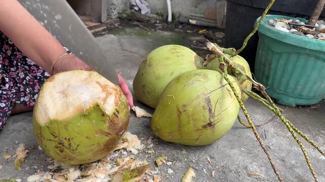 Cutting top of fresh green coconut with machete
