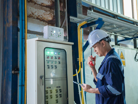 Electrical engineer is communicating with team and use radio while working on digital tablet control electrical panel in industrial plant. System PLC industrial manufacturing. Factory industry 