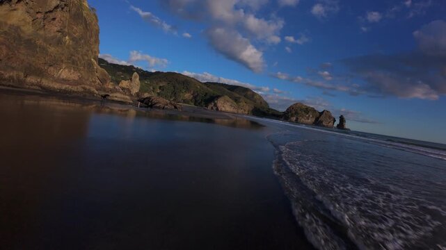 Sunset reflections on wet sand at Piha Beach, New Zealand