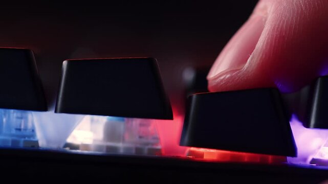 Human finger is clicking on the key on the computer keyboard, close up view. The finger presses  on the gaming keyboard key with led light, macro shot. Loop footage. Low angle.