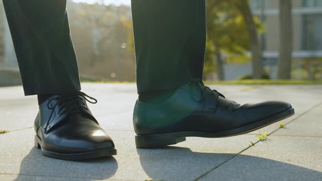 SLOW MOTION: Close-up view to the businessman in a black new shoes and  stamping leg. Legs of a businessman in fashionable shoes. Business concept. Stylish men wears. Low angle.