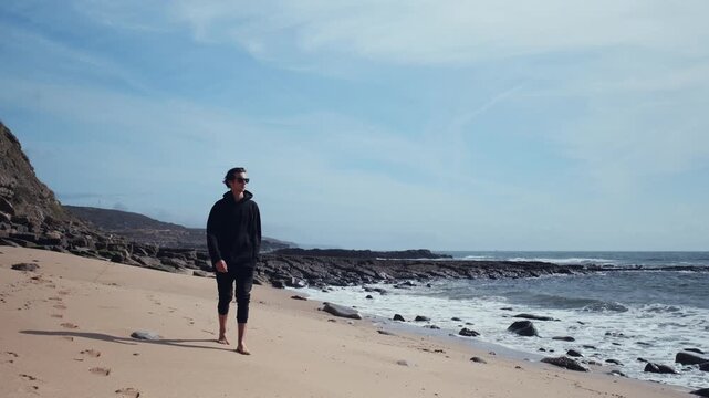 Man with a romantic mood relaxes on the beach contemplating the beautiful nature. Barefoot young man walks on the empty sandy beach on the summer day. Guy  is walking on sandy beach on a sunny day.