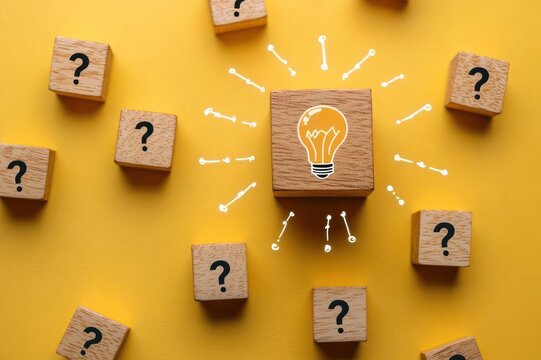 wooden block with drawn light bulb surrounded by wooden blocks printed with question marks on a yellow background, conveying insight, clarity, and optimistic problem solving