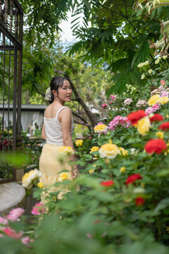 Asian woman turning around smiling in blooming rose garden cafe.