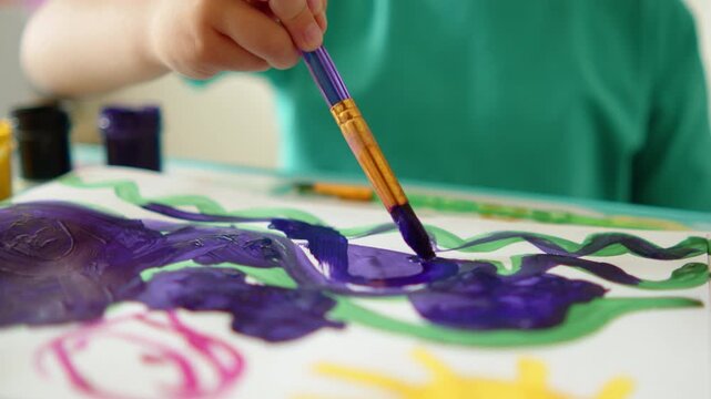 Kid painting a colorful picture, developing creativity in children concept. Close up of a child's hand holding a paintbrush and painting with watercolor. Slow motion.