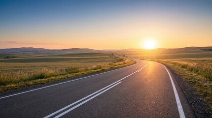 Fototapeta premium Winding asphalt road through golden fields under a bright sunset sky highway