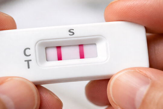 Close up rapid antigen test cassette showing positive result held between fingers