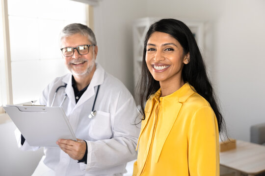 Smiling female patient looks at camera during medical consultation, posing for portrait with reliable male doctor. Visit at hospital, receiving professional healthcare services, health checkup concept
