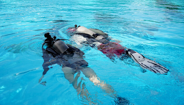 A professional diver and a novice practice diving in a pool.