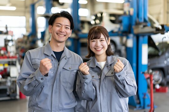 自動車整備工場で働く若い男女が笑顔でガッツポーズ
