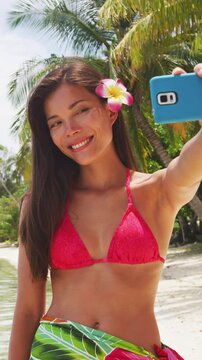 Woman taking phone selfie video or photo. Bikini travel girl on beach smiling happy on Beach, Bora Bora, Tahiti, French Polynesia. Vertical video of real woman model without makeup